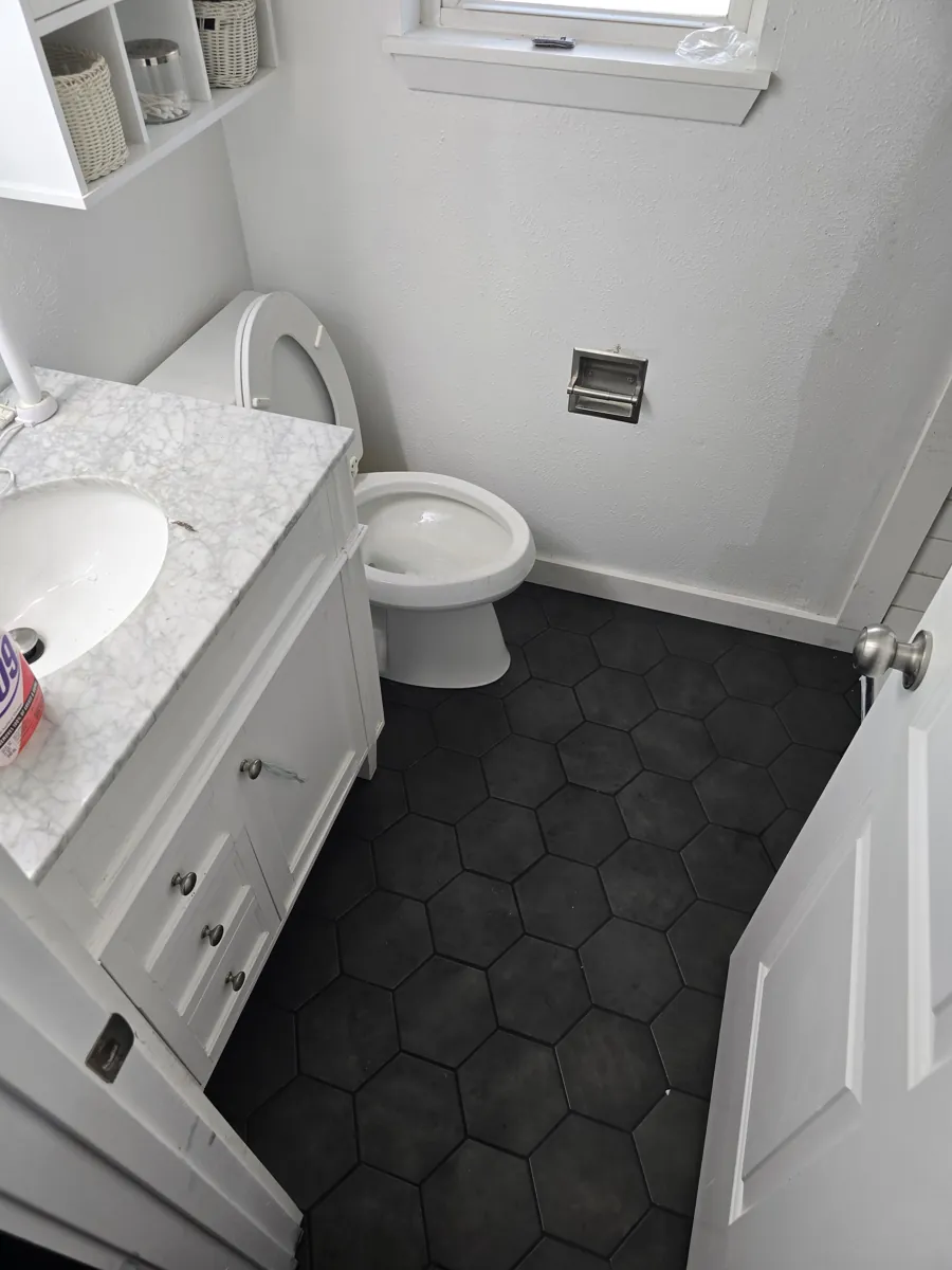 Finished bathroom with black hexagon tile floor, white vanity with marble top, and toilet